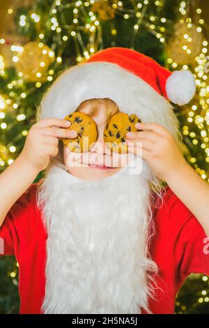 Babbo Natale divertente bambino che raccoglie cookie. Little Babbo Natale che tiene i biscotti di Natale contro gli occhi. Foto Stock