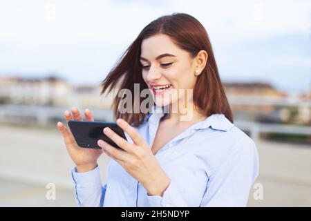 Giovane donna d'affari caucasica redhead messaggi su smartphone e ridere all'aperto Foto Stock