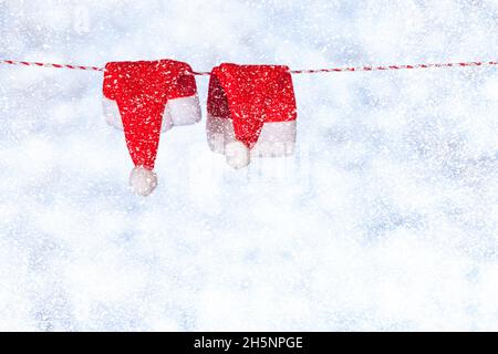 Due cappelli di Natale rossi appendono da una corda contro uno sfondo blu-grigio sfocato lucido. Spazio di copia. Concetto Foto Stock