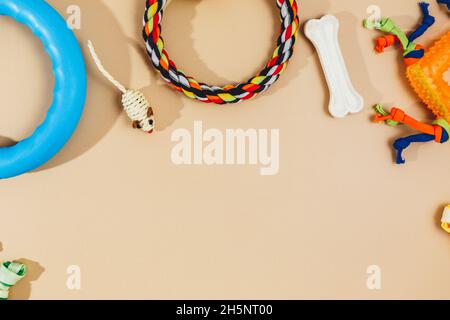 Diversi accessori multicolore per la cura degli animali: Ciotola, ossa, palle, snack, mouse su sfondo beige. Accessori in gomma e tessuto per cani e gatti. Foto Stock