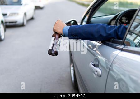 concetto di alcool, guida pericolosa. bere e guidare. l'uomo beve una bottiglia di birra mentre guida l'auto. l'autista getta la bottiglia fuori dall'auto vince Foto Stock