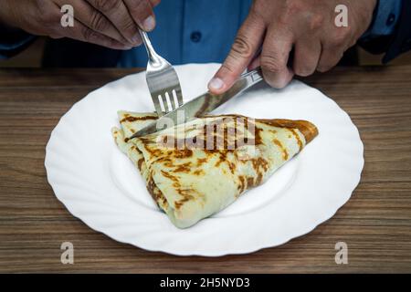 l'uomo con un cucchiaio e una forchetta in mano si prepara per la colazione o il pranzo, il cibo sul tavolo. Un uomo d'affari mangia una frittella durante una pausa pranzo Foto Stock