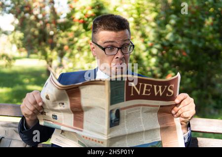 Uomo d'affari senior di successo che legge un giornale finanziario mentre si siede nella piazza della città, all'aperto. Persona sorpresa legge notizie false. Emozione di surpr Foto Stock