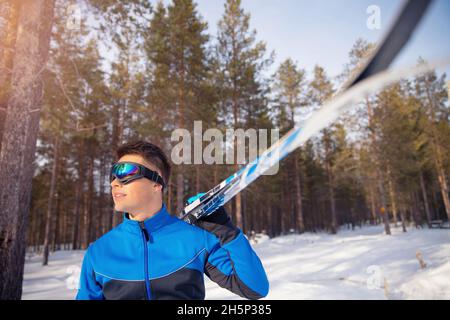 Ritratto di pilota sciatore maschio con sci di fondo sullo sfondo della foresta invernale. Foto Stock