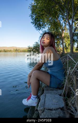 Giovane donna asiatica in luce del sole appled seduta sulla riva di un lago idilliaco Foto Stock