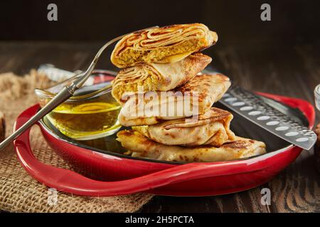 Pancake con carne accatastata con burro e pinze su piatto su sfondo di legno scuro Foto Stock