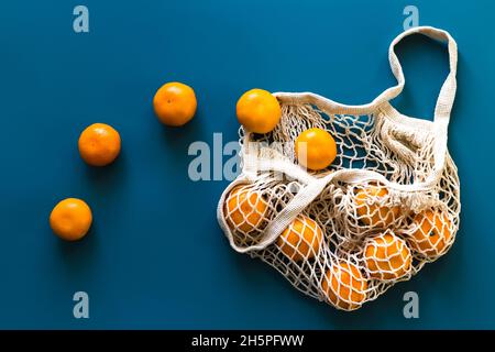 Frutta fresca di mandarini d'arancia in un sacchetto di cotone ecologico a rete su sfondo blu. Concetto di zero rifiuti, shopping senza plastica o cibo ecologico. V superiore Foto Stock