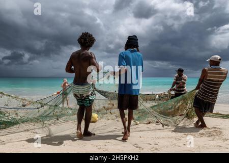 I pescatori tirano le reti dal mare su una spiaggia nei tropici con il cielo drammatico su Mahe Island, Seychelles Foto Stock