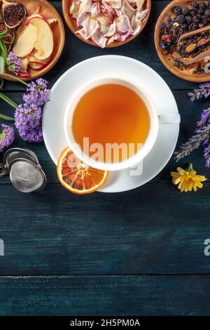 Tè con frutta secca e fiori, girato dalla parte superiore su uno sfondo rustico scuro in legno con un posto per il testo Foto Stock