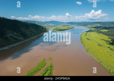 Sorvolando un fiume glaciale in Siberia, Russia, con montagne verdi e binari ferroviari sullo sfondo. Foto Stock