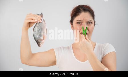 Donna caucasica con un vestito sul naso a causa dell'odore disgustoso di pesce. Una metafora per la salute e l'igiene intima delle donne. Foto Stock