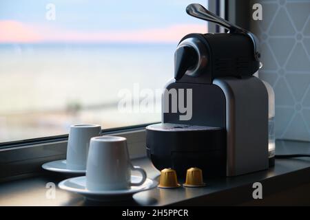 Macchina da caffè con capsule e due tazze pronte per essere utilizzate vicino a una finestra. Foto Stock