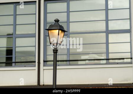 lampione illuminato, sullo sfondo delle finestre di un edificio moderno, nella città metropolitana. Foto Stock