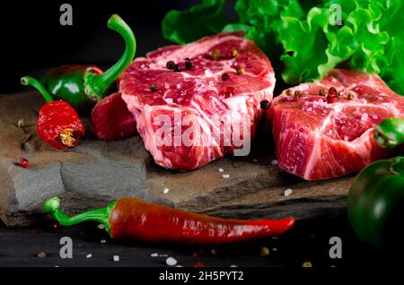 Cibo impostato per un pic-nic. Bistecche di manzo ribeye pronto per cucinare al barbecue. Due classiche bistecche di ribeye fresche su pietra con erbe di pepe in grani su pietra grigia Foto Stock
