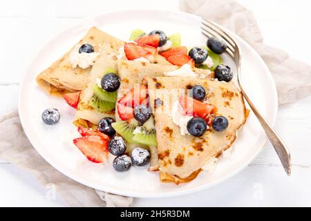 Crepes dolce con frutti di bosco e crema su sfondo bianco di legno. Concetto di cibo fatto in casa. Foto Stock