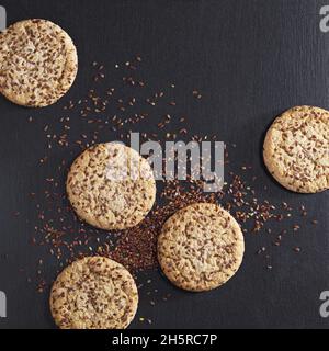 Round i cookie con sesamo e semi di lino in pietra nera di sfondo, vista dall'alto Foto Stock