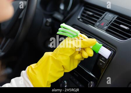 Una mano in guanti di gomma gialli pulisce il cruscotto di un'automobile dalla polvere con una spazzola speciale in una giornata d'autunno brillante. Messa a fuoco selettiva. Primo piano Foto Stock