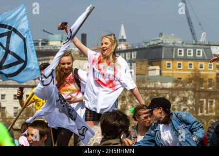 Foto di strada di un gruppo di giovani manifestanti del cambiamento climatico che ballano con una giovane donna centrale e simboli e bandiere della ribellione di estinzione. Foto Stock