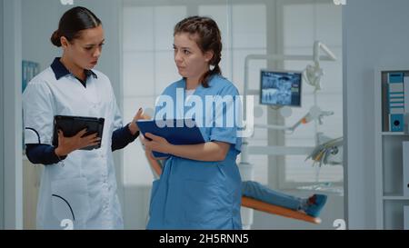 Il team di lavoro degli ortodontisti che discute il funzionamento dentale presso la clinica. Dentista e assistente in piedi in cabina stomatologica mentre si parla di apparecchiature orali e di esame dei denti Foto Stock