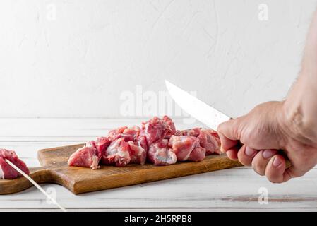 Pezzi di carne cruda affettati su un tagliere su sfondo bianco di legno. Carne di maiale o di manzo preparata per cucinare. Foto Stock