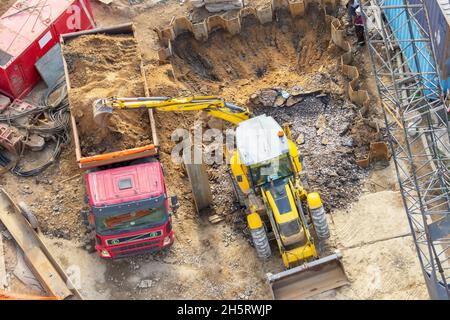 L'escavatore scava un foro e carica il terreno nella parte posteriore di un camion, vista dall'alto aerea Foto Stock