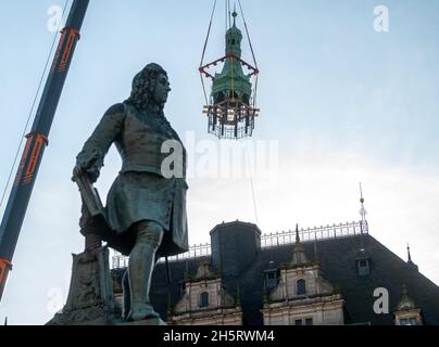 11 novembre 2021, Sassonia-Anhalt, Halle (Saale): Il casco torre della casa cittadina di Halle/Saale si aggancia sul gancio della gru dietro il monumento Handel dall'edificio al mercato. Lo storico Stadthaus è attualmente in fase di ristrutturazione. Nel corso dei lavori sulle capriate del tetto e sul soffitto in stucco nella sala banchetti, è stato ora smantellato anche il casco della torre pendente rivestito di lenzuola di rame. Durante i lavori sull'edificio, la torre si trova nel cortile interno della casa cittadina. L'edificio neo-gotico neo-rinascimentale per riunioni e festival è stato inaugurato nel 1894. Nel 1903, il Germ Foto Stock