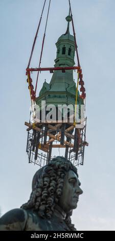 11 novembre 2021, Sassonia-Anhalt, Halle (Saale): Il casco torre della casa cittadina di Halle/Saale si aggancia sul gancio della gru dietro il monumento Handel dall'edificio al mercato. Lo storico Stadthaus è attualmente in fase di ristrutturazione. Nel corso dei lavori sulle capriate del tetto e sul soffitto in stucco nella sala banchetti, è stato ora smantellato anche il casco della torre pendente rivestito di lenzuola di rame. Durante i lavori sull'edificio, la torre si trova nel cortile interno della casa cittadina. L'edificio neo-gotico neo-rinascimentale per riunioni e festival è stato inaugurato nel 1894. Nel 1903, il Germ Foto Stock