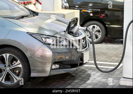 Nissan Leaf viene caricato presso il punto di ricarica rapida EV per i veicoli elettrici. L'auto elettrica viene caricata tramite cavo. Foto Stock