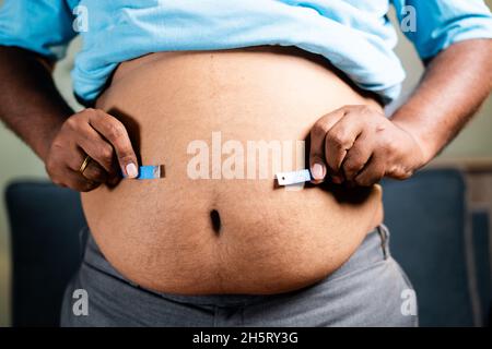 L'uomo obeso non sano e irriconoscibile controlla il grasso dello stomaco o della vita usando il nastro di misurazione prima della dieta a casa - concetto di sofferenza del corpo sovrappeso dovuto Foto Stock