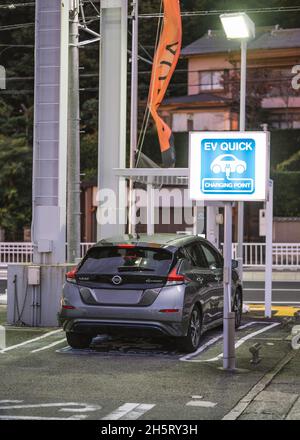 Nissan Leaf viene caricato presso il punto di ricarica rapida EV per i veicoli elettrici. Segnale di accensione della luce blu. Foto Stock