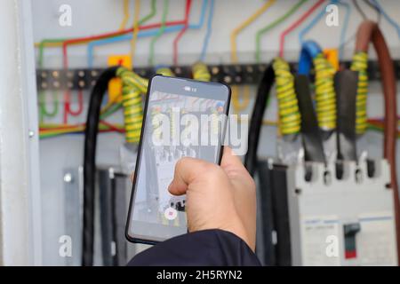 Tecnico che esegue la lettura del contatore elettrico di Kilowatt-ora utilizzando smartphone, tariffe diurne e notturne in kilowatt Foto Stock
