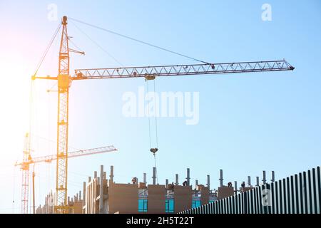 Alta gru da costruzione sullo sfondo di un edificio residenziale incompiuto a più piani e multi appartamenti Foto Stock