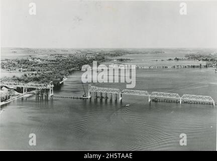 Wisconsin - Minnesota Interstate Highway Bridge sulla U.S. 12. Una vista aerea dell'intero ponte che guarda a nord, o a monte. Il vecchio ponte a pedaggio e il ponte ferroviario Omaha sullo sfondo. La costa del Minnesota a sinistra dell'immagine. La costruzione del ponte lungo quasi mezzo miglio che attraversa il fiume St. Croix è in fase di completamento, 5/22/1951. (Foto di Bureau of Public Roads) Foto Stock