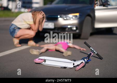 Bambina si trova immobile su asfalto con scooter dopo collisione con auto Foto Stock