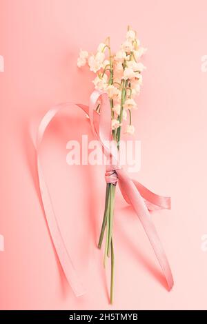 Giglio della valle bouquet legato con un nastro rosa su sfondo rosa. Delicato concetto di primavera Foto Stock