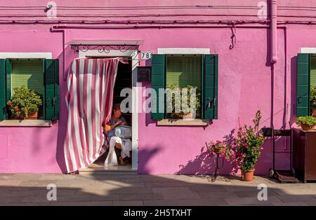 Donna che fa ricamo all'ingresso di una casa colorata, Burano, Venezia, Italia Foto Stock