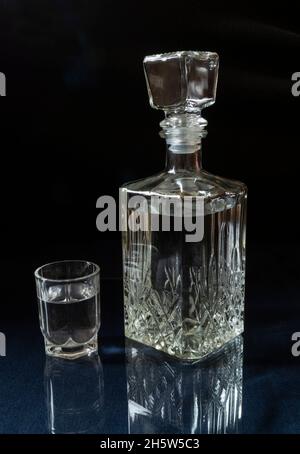 Vodka in un decanter e un bicchiere sul tavolo con un riflesso. Cibo su sfondo nero Foto Stock