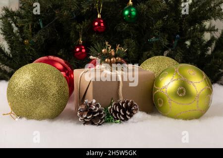 Scatola regalo di Natale decorata con sfere colorate su neve finta, sullo sfondo un albero di Natale con lampade pendenti, decorazione per le vacanze Foto Stock