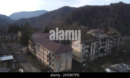 Vista aerea degli antichi edifici residenziali abbandonati circondati da montagne con alberi. Vecchio insediamento in cima alla collina di montagna. Foto Stock