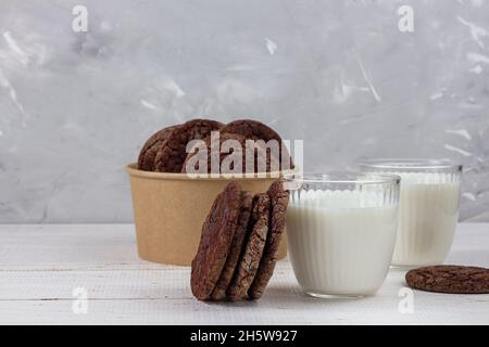 Delizioso latte fresco su un vecchio sfondo di legno. Una caraffa di latte e una bottiglia di latte. Biscotti con gocce di cioccolato. Imballaggio ecologico. Spazio per la copia Foto Stock