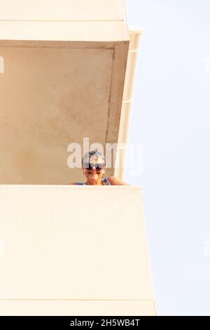 donna di mezza età in occhiali da sole che sbuccia sopra il balcone dell'hotel e sorridente può Pastilla Mallorca Spagna Foto Stock