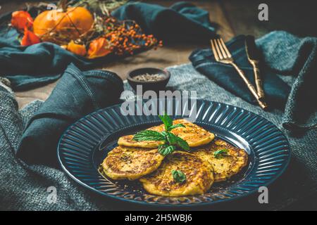 Piccole frittelle di zucca con erbe su un piatto blu su sfondo blu e legno Foto Stock