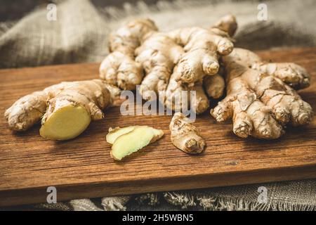 Zenzero fresco su un asse di legno, radici intere e fette tagliate Foto Stock