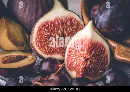 Frutti di fine estate: Metà fico e prugna, insieme all'uva. Mettere a fuoco sulla fig. Primo piano. Foto Stock