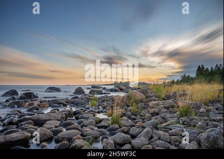 Lunga esposizione di un magnifico tramonto morbido e colorato vicino alla pietra del mare. Bel movimento nube con pietre di mare. Foto Stock