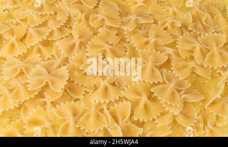 Pasta secca non cotta con bow-tie come sfondo culinario giallo. Primo piano di uova crude farfalle di farina di grano impasto bella consistenza. Mucchio di pasta di farfalla. Foto Stock