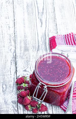 Marmellata di lamponi in vaso di vetro su tavolo di legno bianco Foto Stock