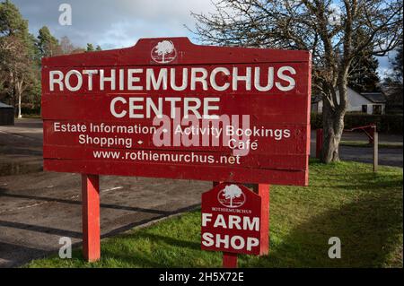 Insegna rossa e bianca per il centro Rothiemurchus e il negozio di fattoria. Giorno di sole, nessuna gente. Segno isolato con sfondo sfocato di erba, alberi, cielo blu nube Foto Stock