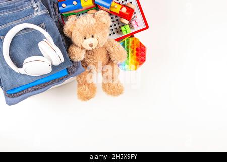 Donazione, concetto di carità. Scatole per donazioni con abbigliamento e giocattoli per bambini su un tavolo bianco. Vista dall'alto, spazio di copia Foto Stock