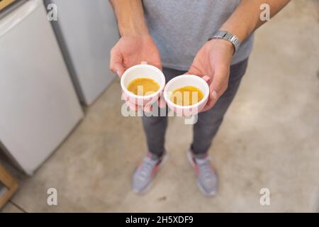Coltivare anonimo barista maschile in abbigliamento casual mostrando tazze di caffè caldo mentre si trova in piedi in leggera moderna caffetteria durante il lavoro Foto Stock